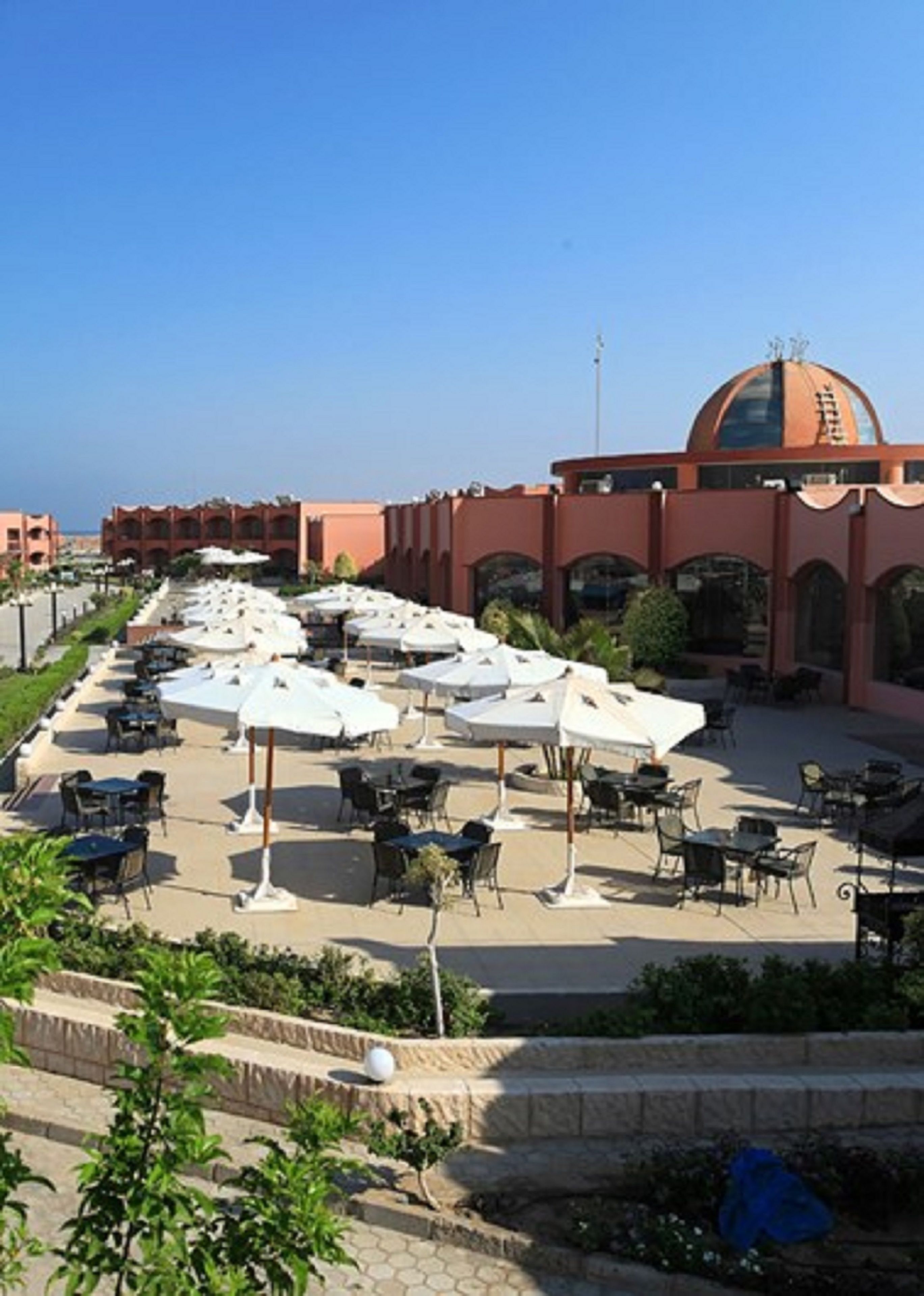An outdoor dining area with tables and umbrellas, a large building with a dome in the background, and a clear sky.