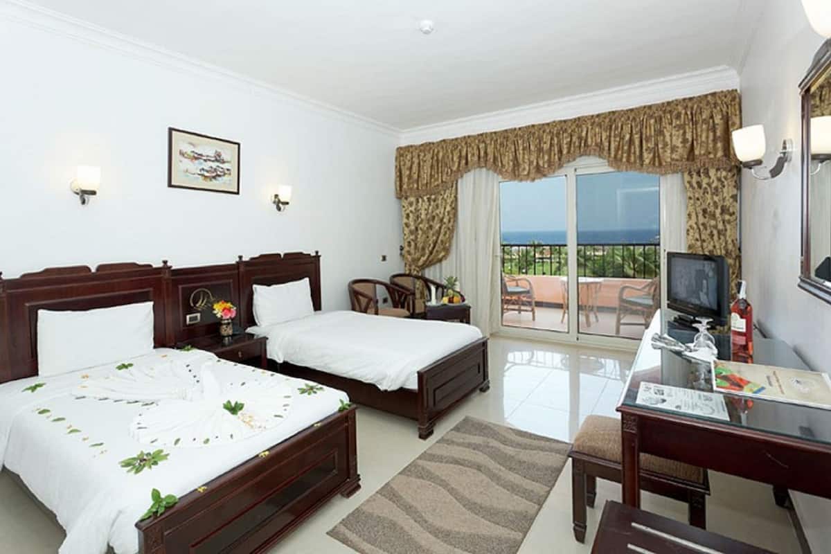 A hotel room with two beds, a desk with a television, a balcony with a view, and a painting on the wall.