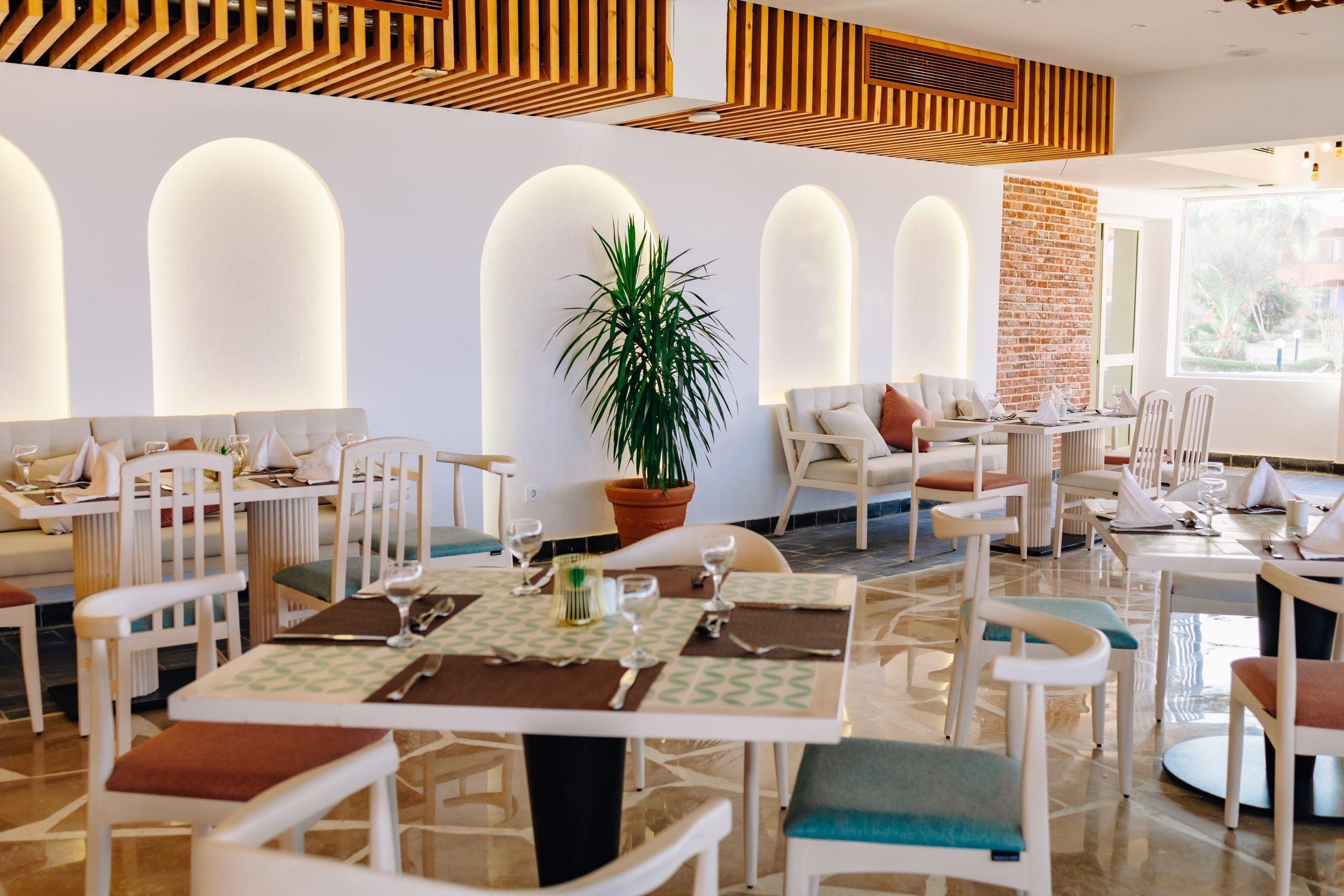 Un comedor moderno con mobiliario blanco, una planta en maceta en el centro y una pared de ladrillo.