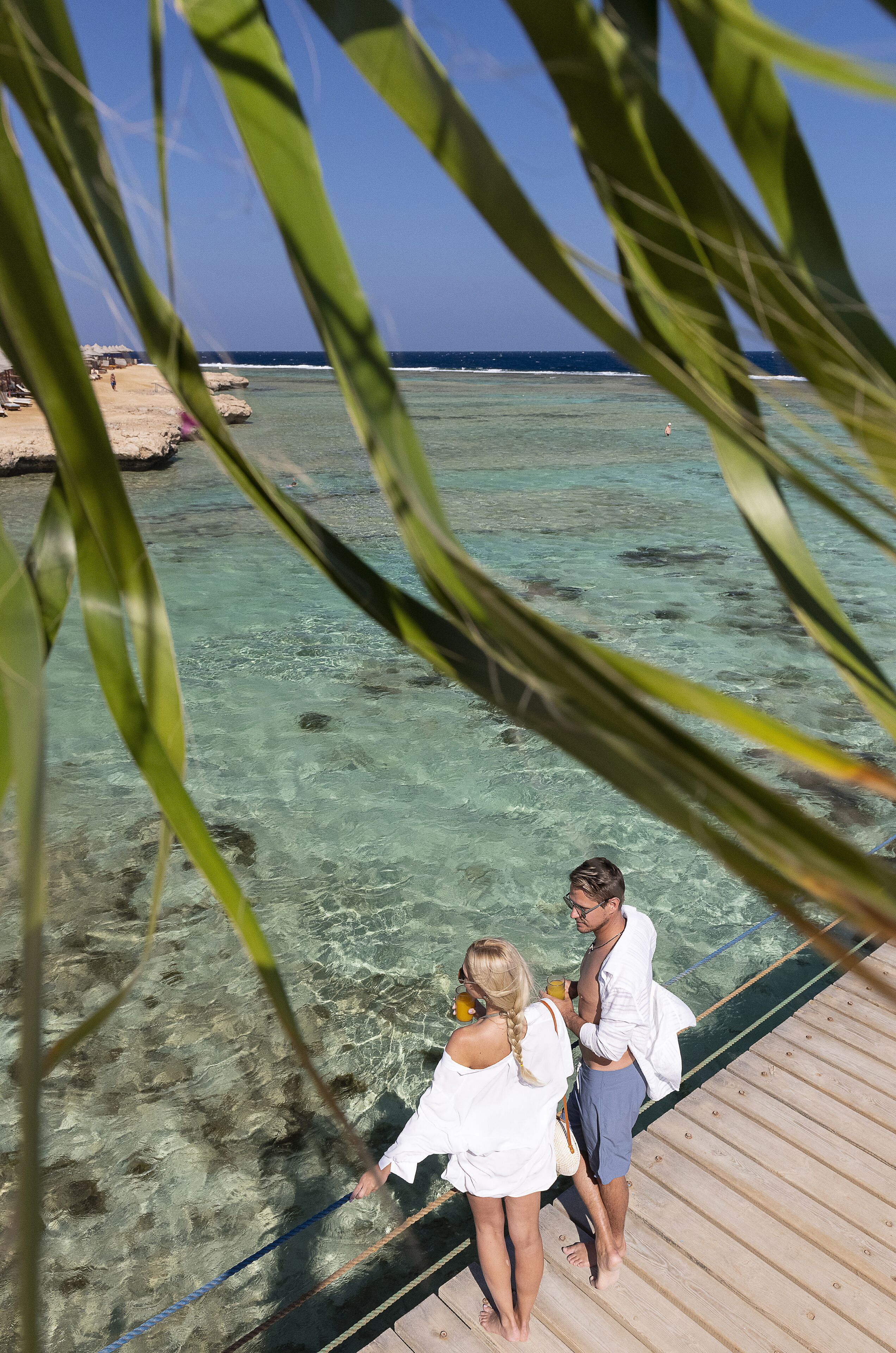 A wooden deck overlooking clear turquoise water with visible rocks and a distant shoreline.