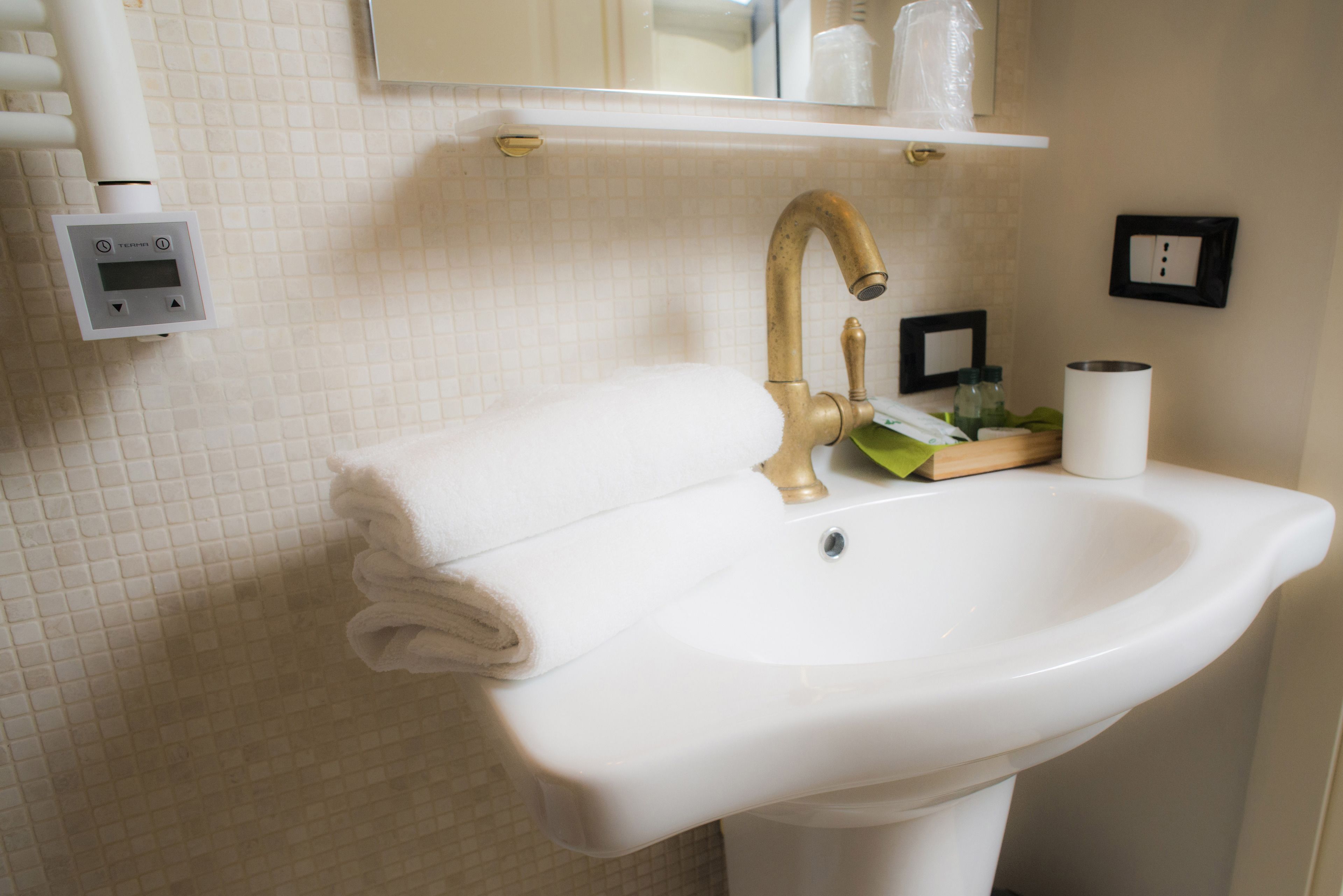 A bathroom with a white sink, a gold faucet, a towel, a soap dispenser, and a mirror.