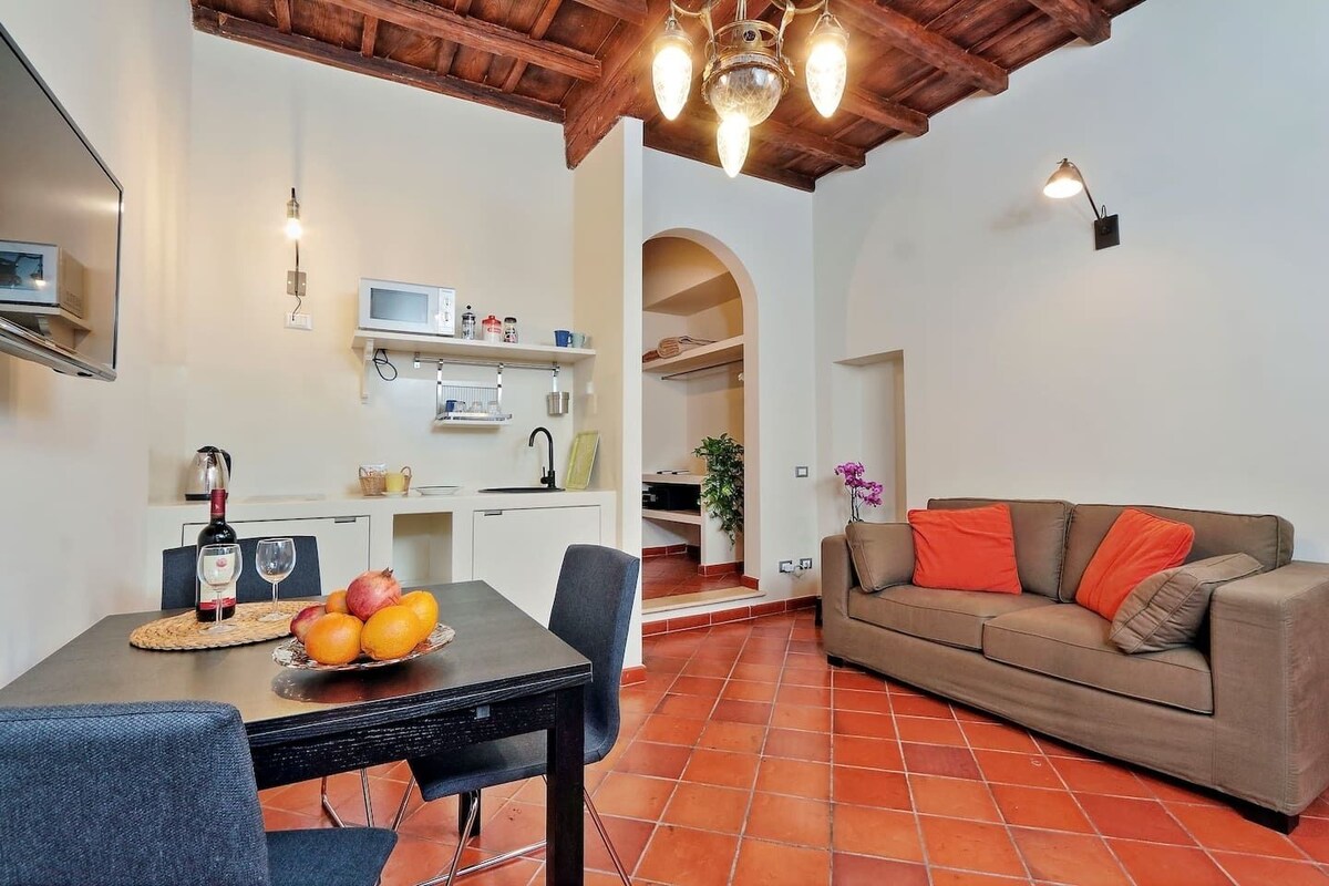Un comedor con una mesa preparada para dos personas, un sofá y una cocina al fondo.