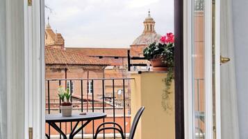 A balcony with a table and chairs, a potted plant, and a view of buildings with domed roofs.