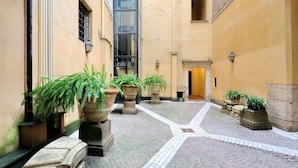 A narrow courtyard with tiled flooring, potted plants, and a building entrance. - CancelleriaDieci (Rome)