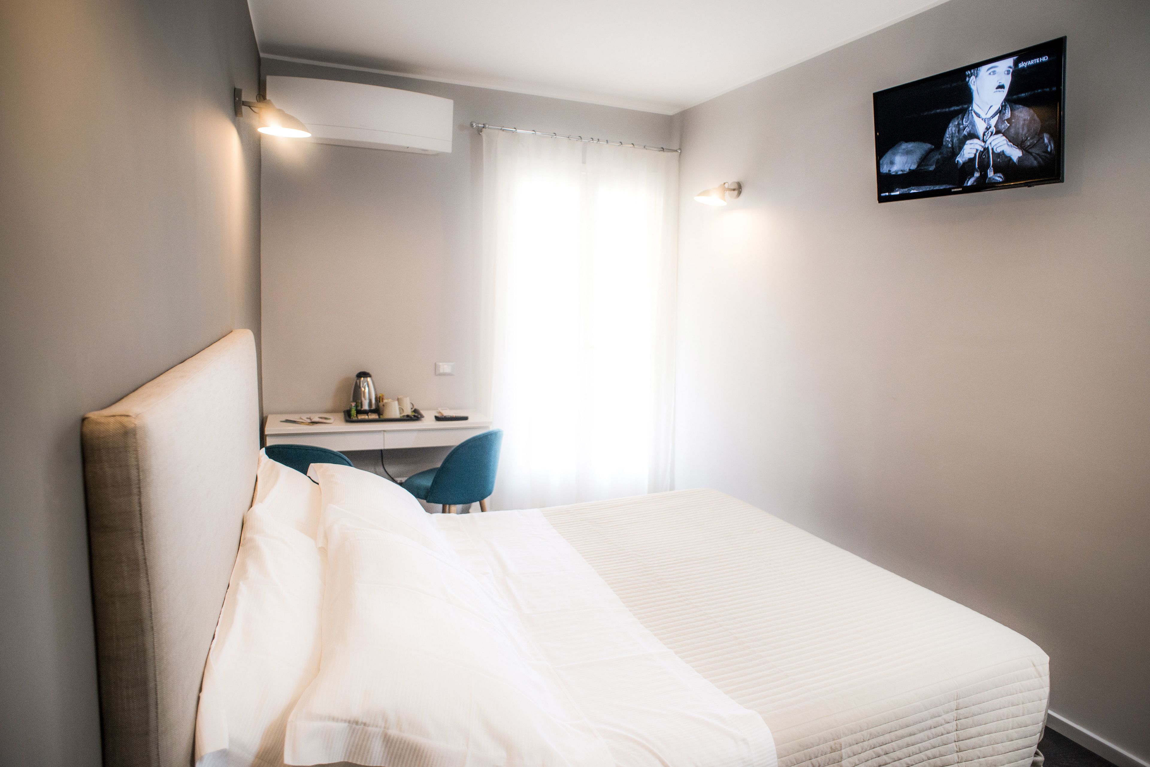 Una habitación de hotel con una cama, un escritorio, una silla y un televisor montado en la pared.