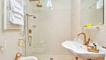 Een badkamer met een douche met glazen wanden, een witte wastafel met gouden details en een spiegel boven de wastafel.
