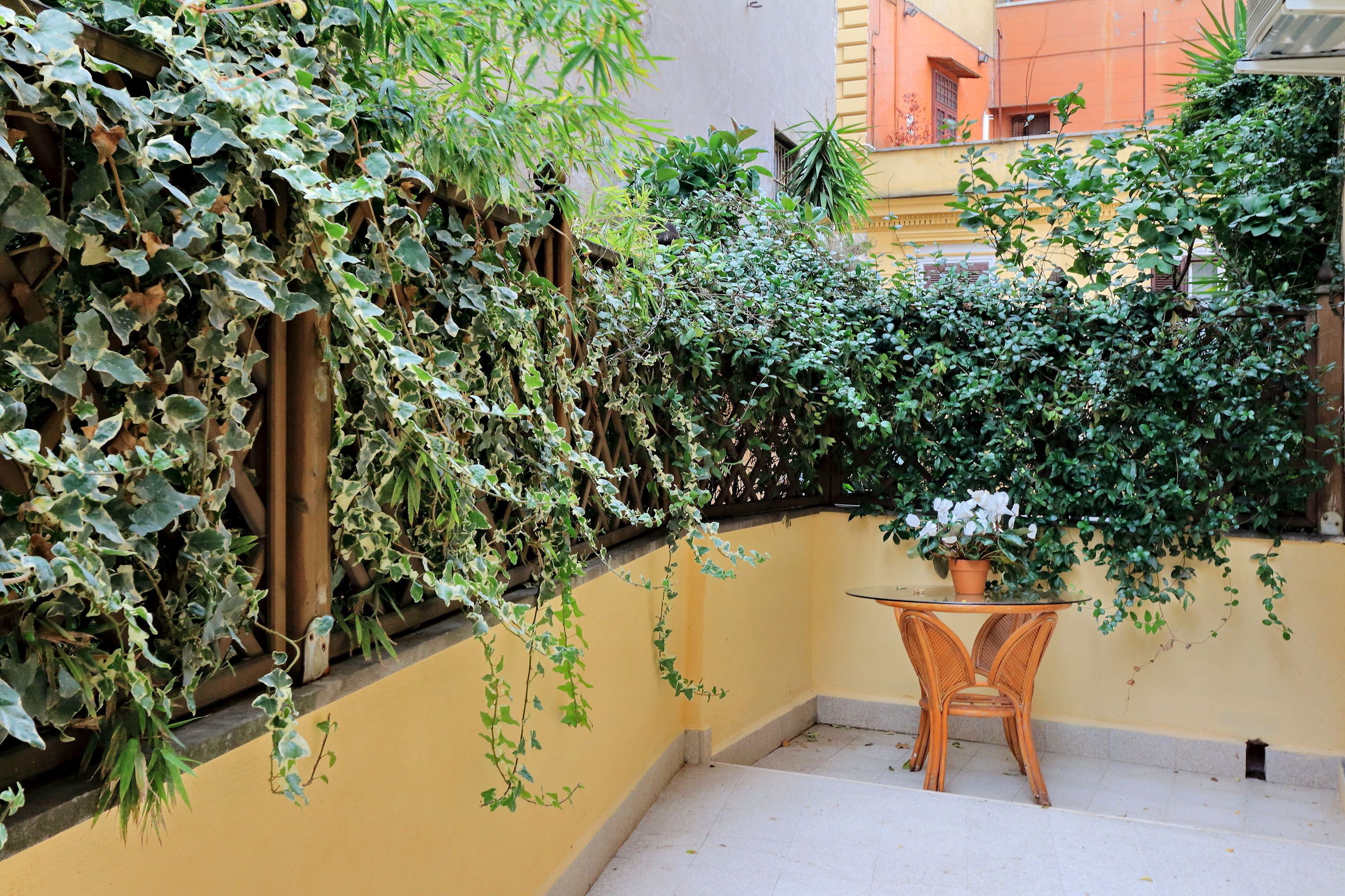 A small outdoor area with a yellow wall, a wooden fence, and a table with chairs.
