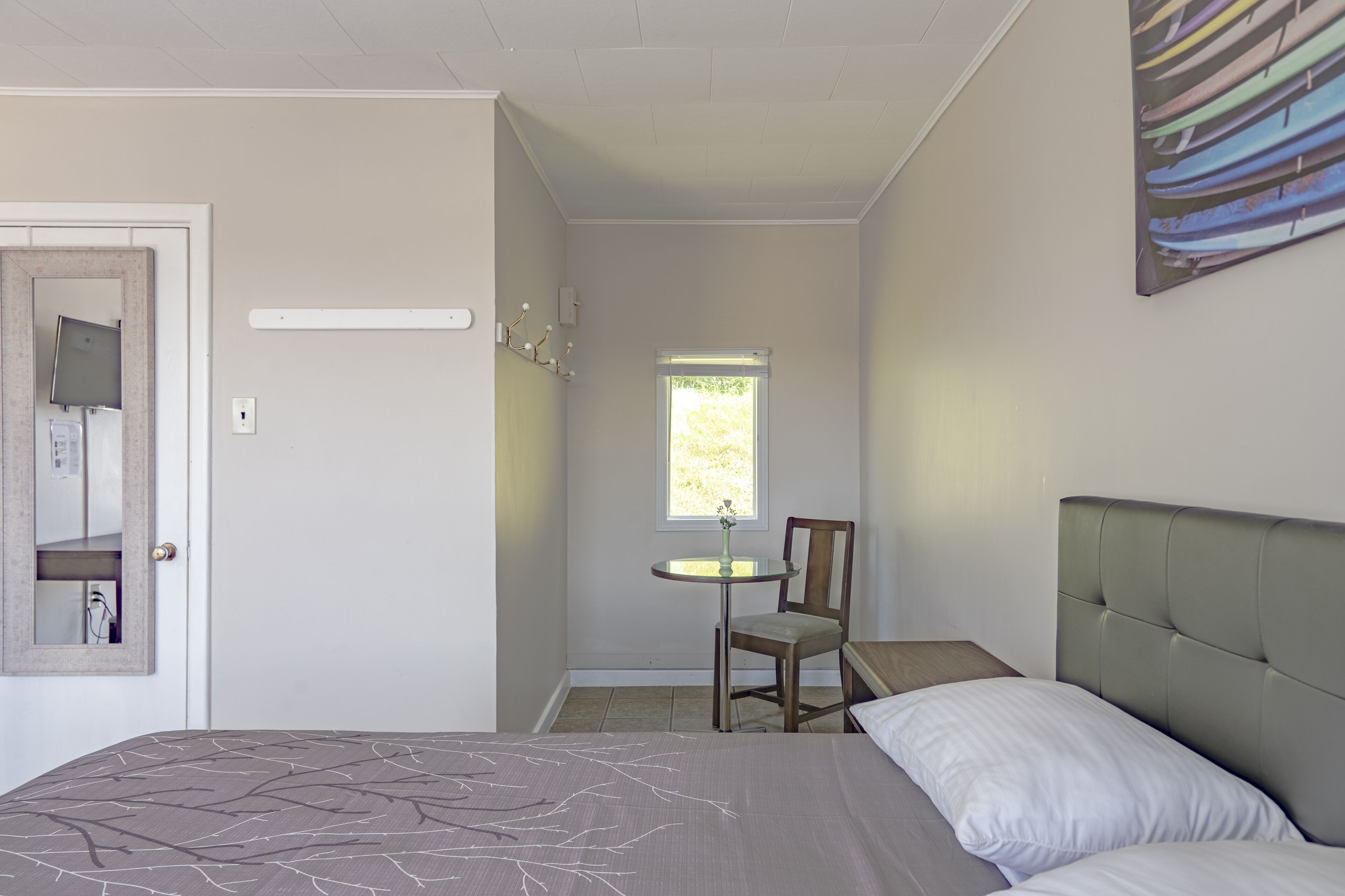 Una camera da letto con un letto, una sedia, un tavolino con un vaso, una finestra e un punto luce a parete.