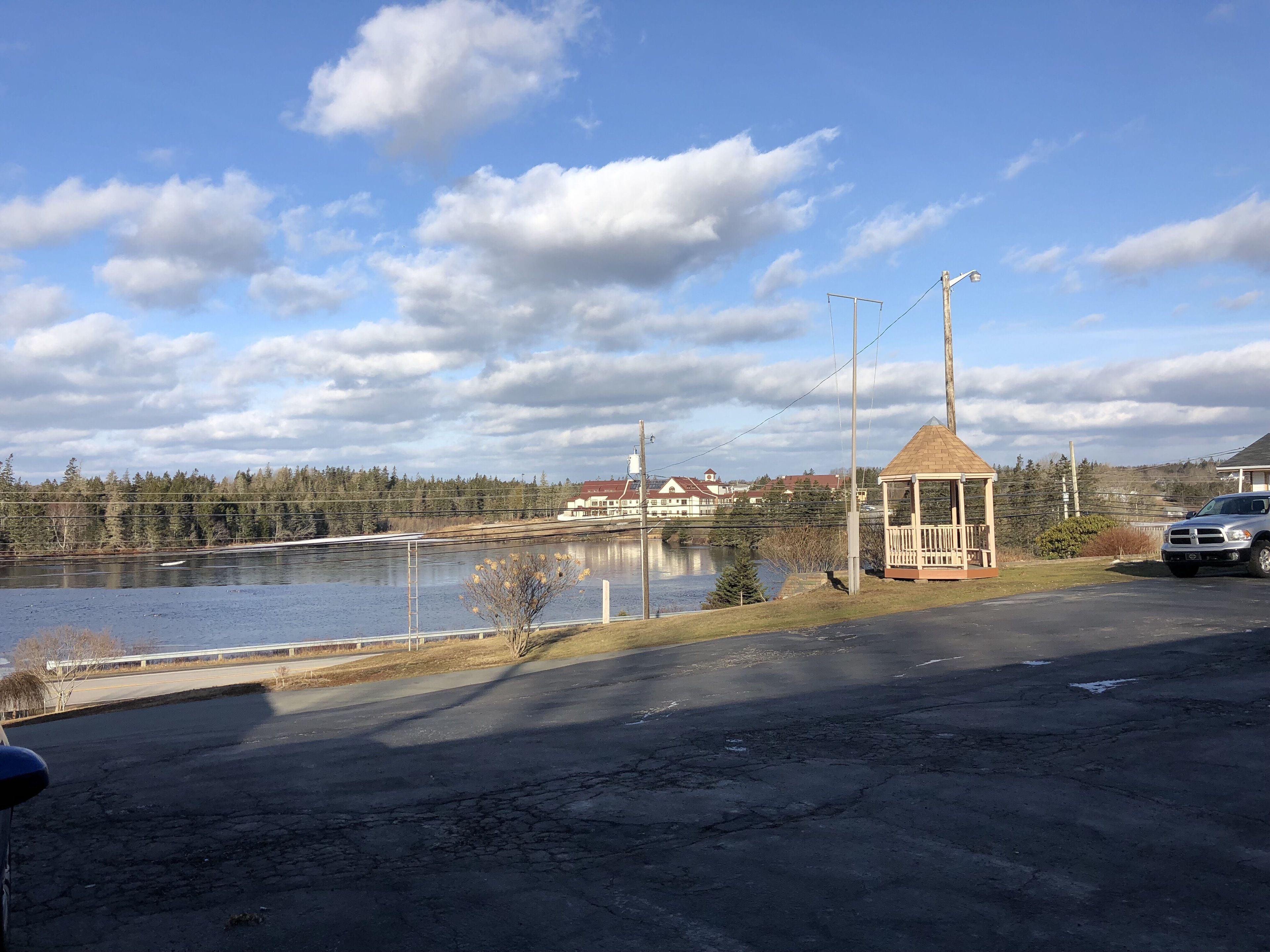 A gazebo, a body of water, and a building with a red roof in the background.