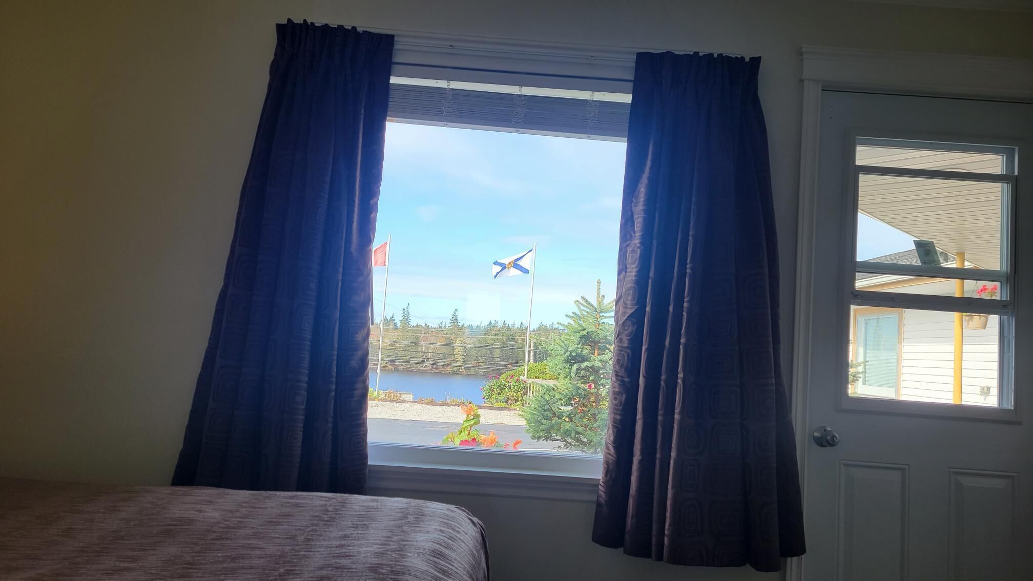 Una habitación con una cama, una ventana con cortinas y vistas a una bandera y una masa de agua.
