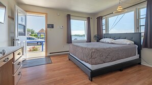 A bedroom with a bed, a dresser, a window with curtains, and a view of the outside. - NovaStar Motel On The Lake (Dayton)