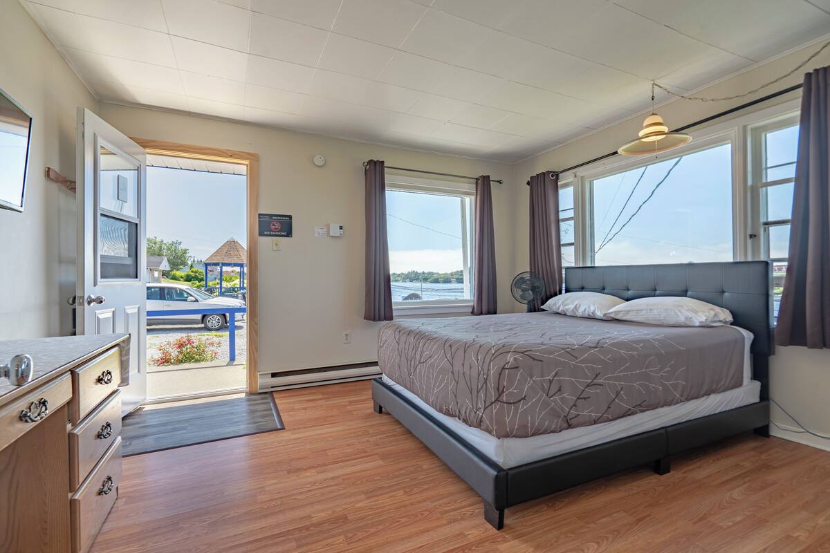 Un dormitorio con cama, cómoda, ventana con cortinas y vistas al exterior.