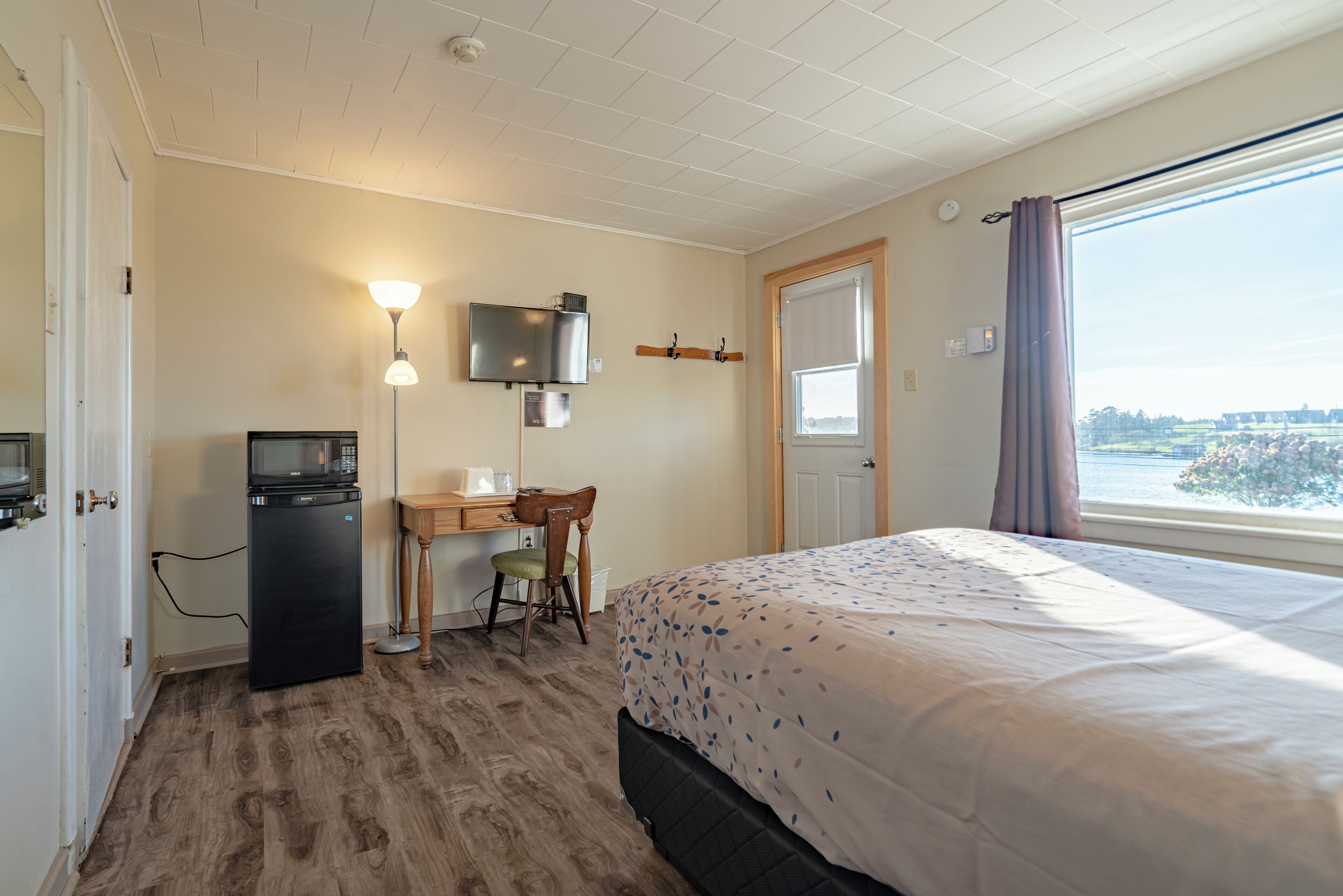 Een hotelkamer met een bed, bureau, stoel, televisie en een raam met gordijnen.