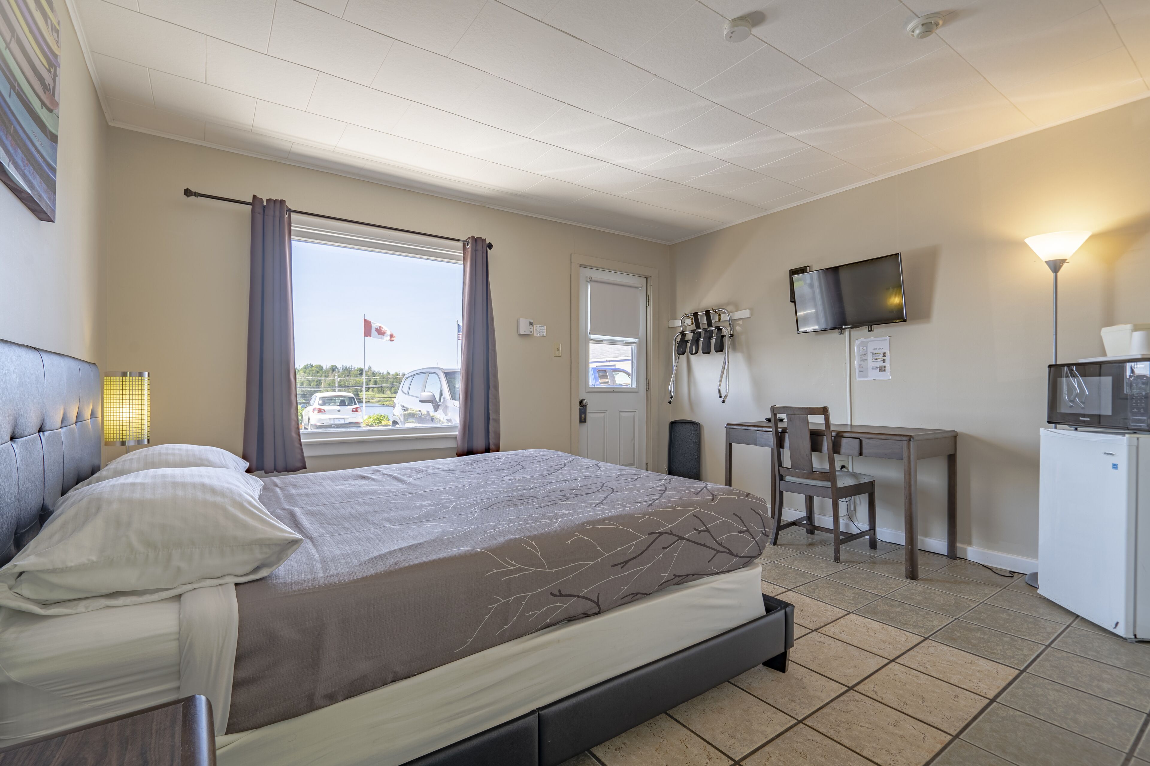 A hotel room with a bed, a desk, a chair, a television, and a refrigerator.