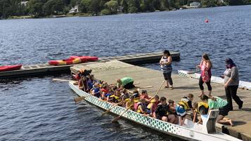 Een drakenboot met kinderen en volwassenen aan een steiger, omringd door rustig water en bomen.