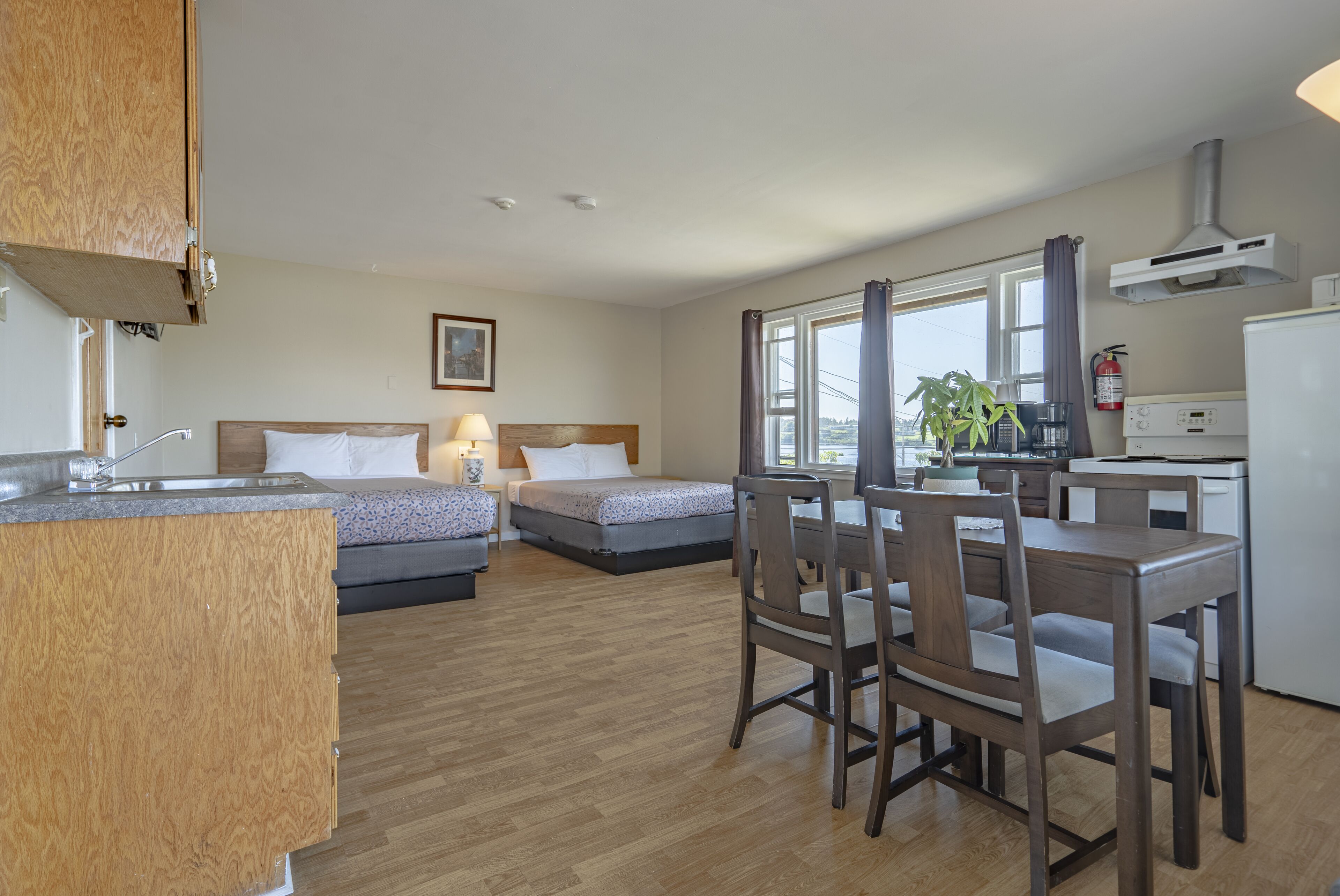 Una habitación pequeña con cama, mesita de noche, lámpara y una kitchenette.