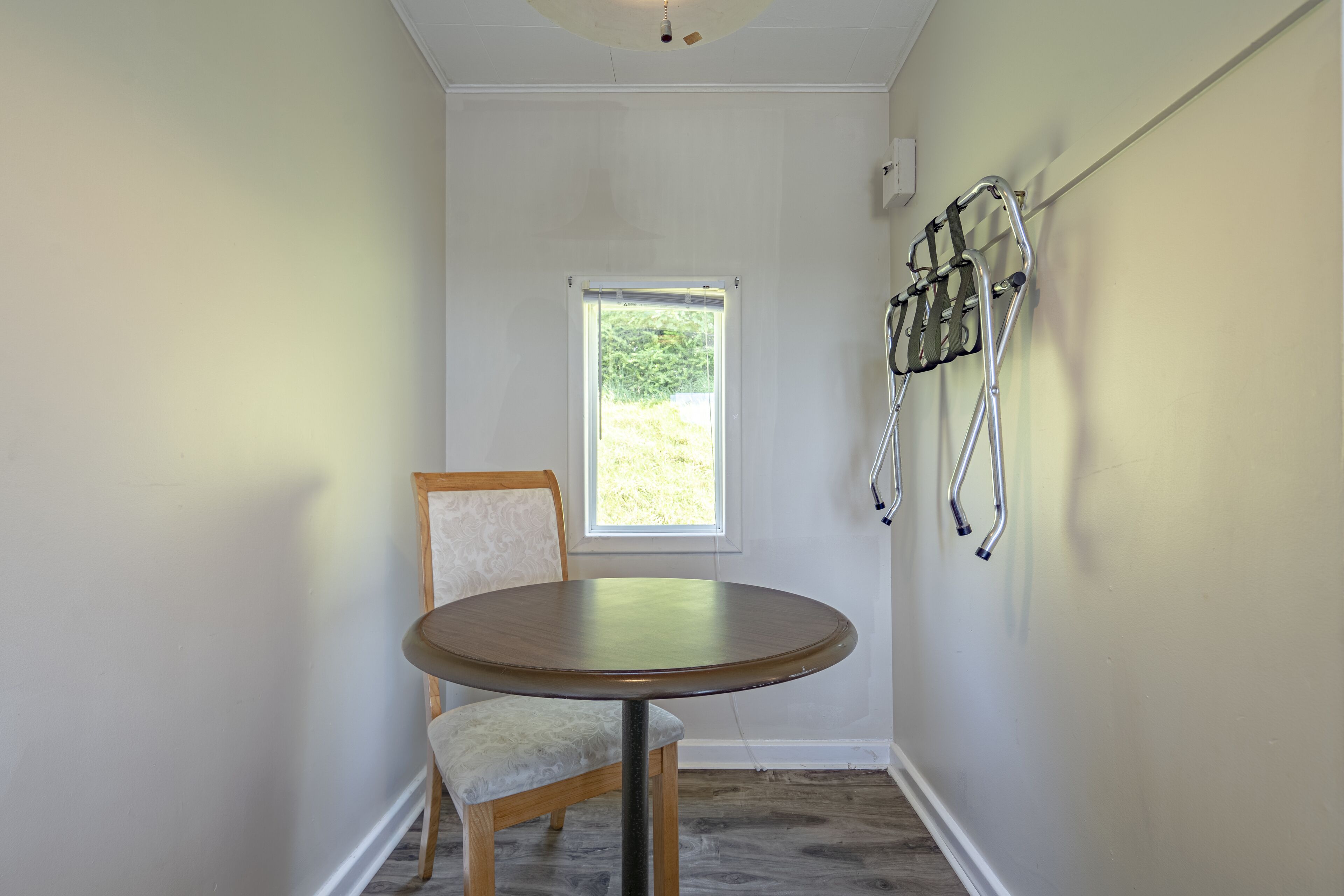 A room with a round table, a chair, a window, and a wall-mounted handrail.