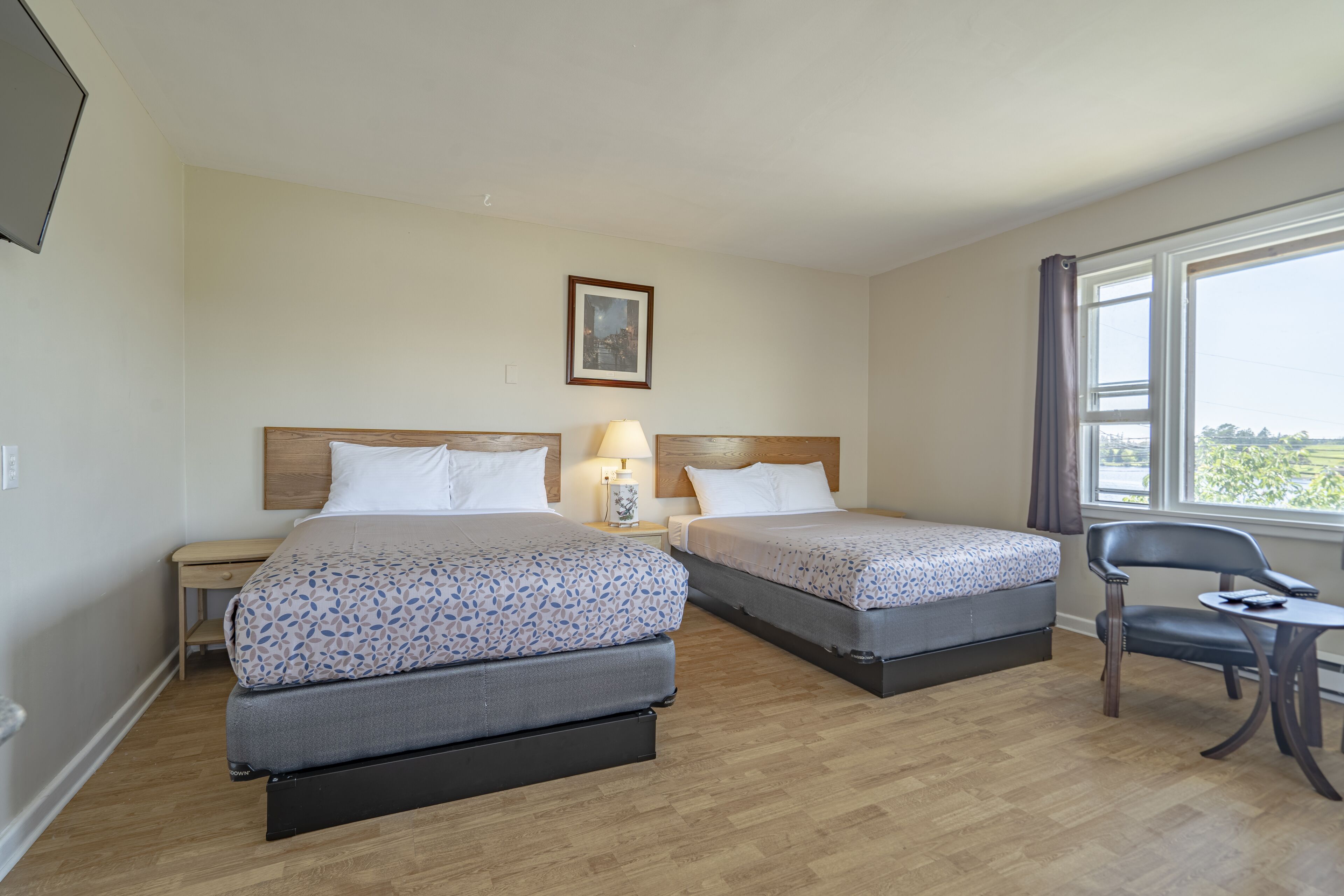 Une chambre d’hôtel avec deux lits, une chaise, une petite table, une lampe et un tableau au mur.