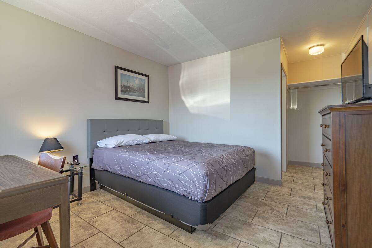 Un dormitorio con cama, mesita de noche, lámpara y un cuadro en la pared.