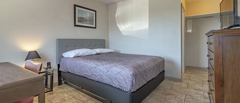 Un dormitorio con cama, mesita de noche, lámpara y un cuadro en la pared.
