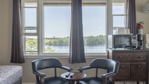 A room with two chairs, a small table with remotes, a bed, a desk with a microwave, and a view of a lake. - NovaStar Motel On The Lake (Dayton)