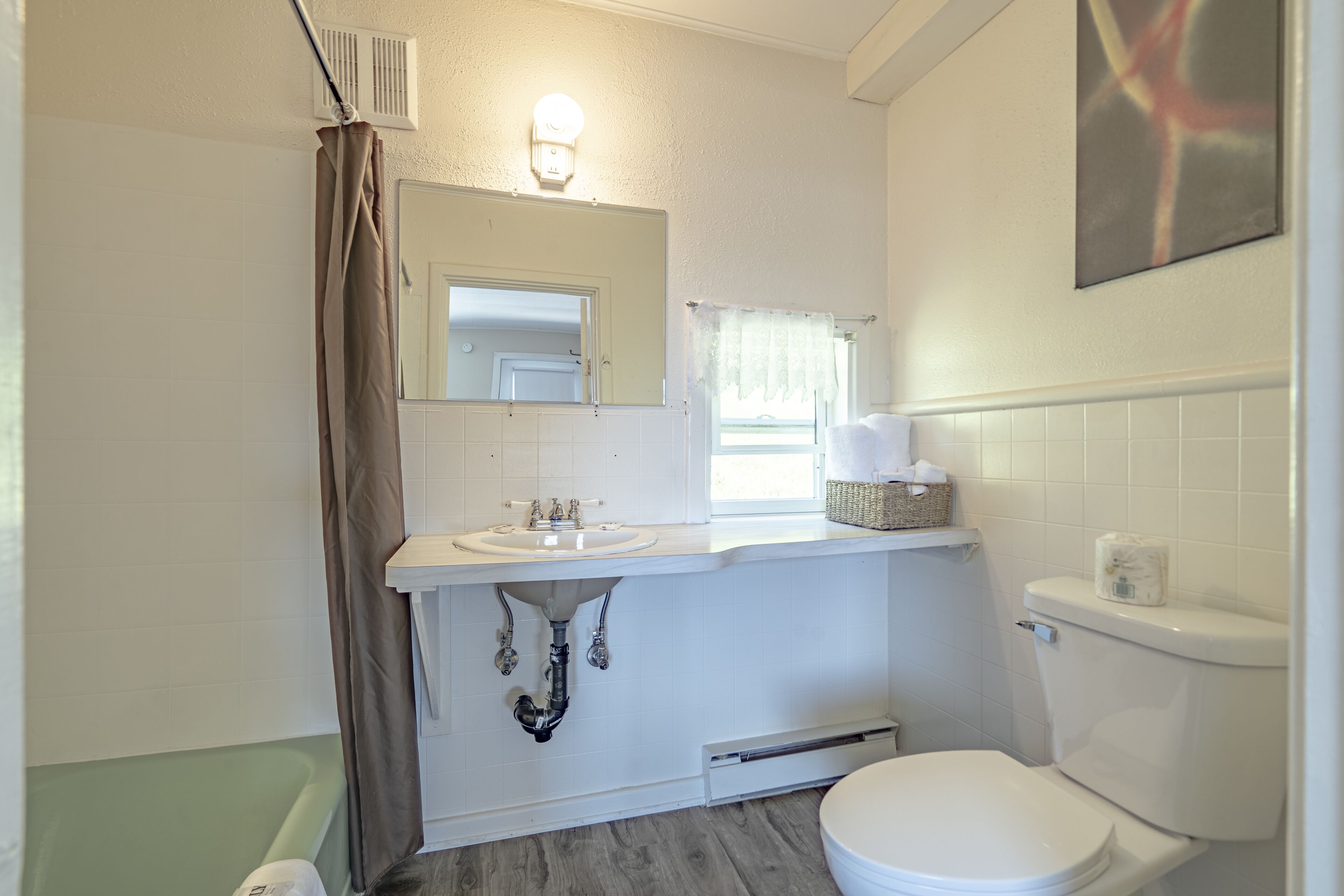 Une salle de bain avec un lavabo blanc, un miroir et des toilettes, une fenêtre avec un rideau et un luminaire au-dessus du miroir.