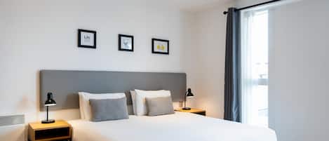 Ein modernes Hotelzimmer mit einem großen Bett, zwei Nachttischen mit Lampen und drei gerahmten Bildern an der Wand.