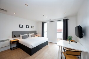 A modern hotel room with a large bed, a desk with a chair, a TV, and a window with curtains.