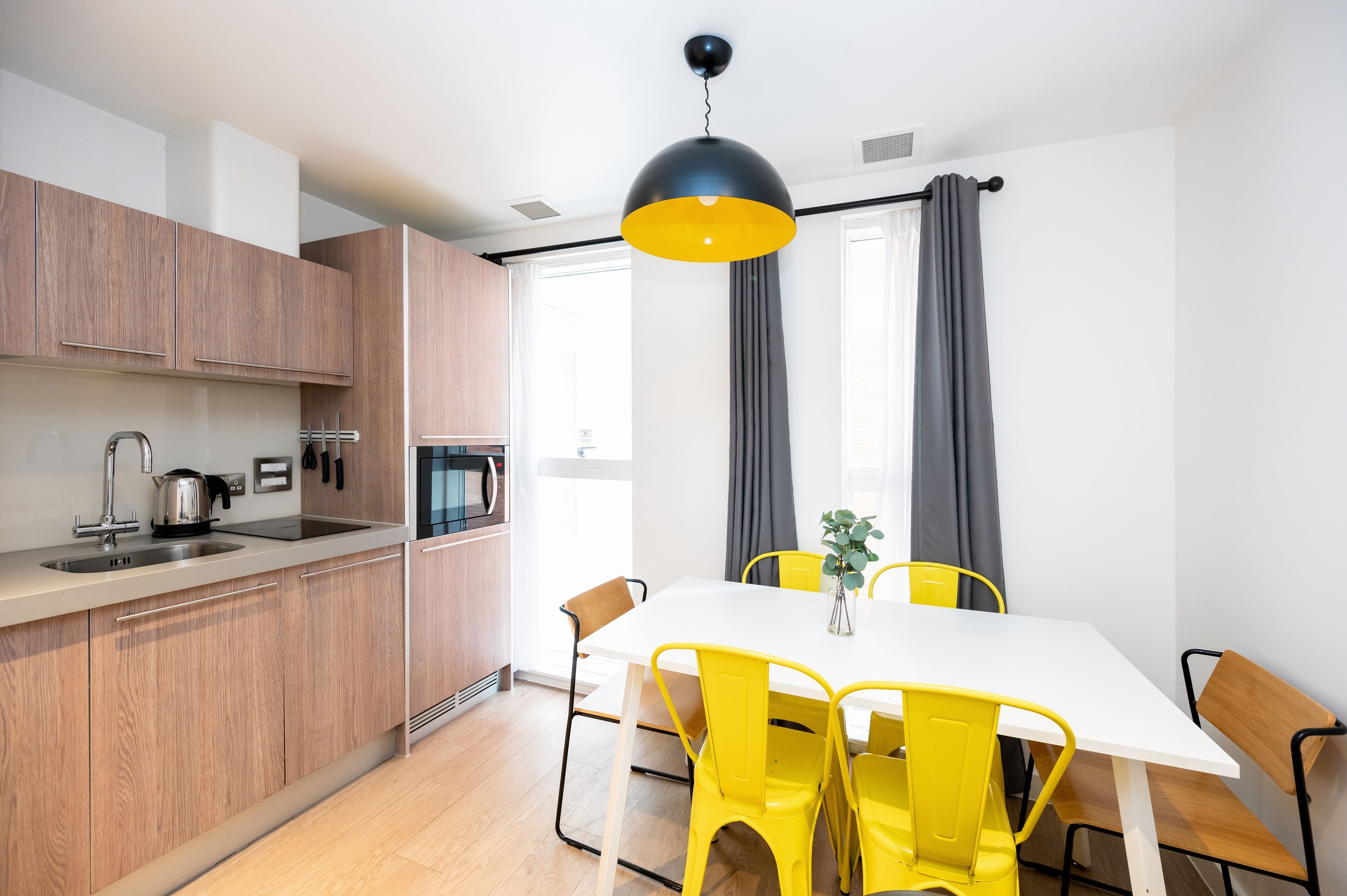 A modern kitchen with wooden cabinets, a white countertop, and a black pendant light.
