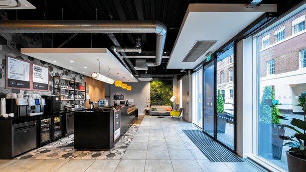 Interior de cafeteria moderna amb taulell de recepció, zona de seients i grans finestres que donen a la vista del carrer.