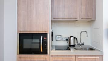 Une cuisine moderne avec des meubles en bois, un four à micro-ondes encastré, une bouilloire et un évier en acier inoxydable.