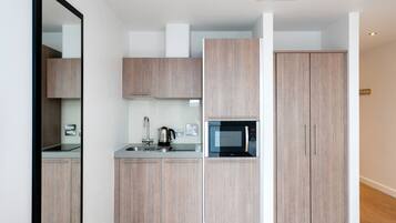 A modern kitchen with light wood cabinets, a built-in microwave, and a kettle.