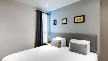 A modern hotel room with a large bed, a nightstand with a lamp, and framed pictures on the wall.