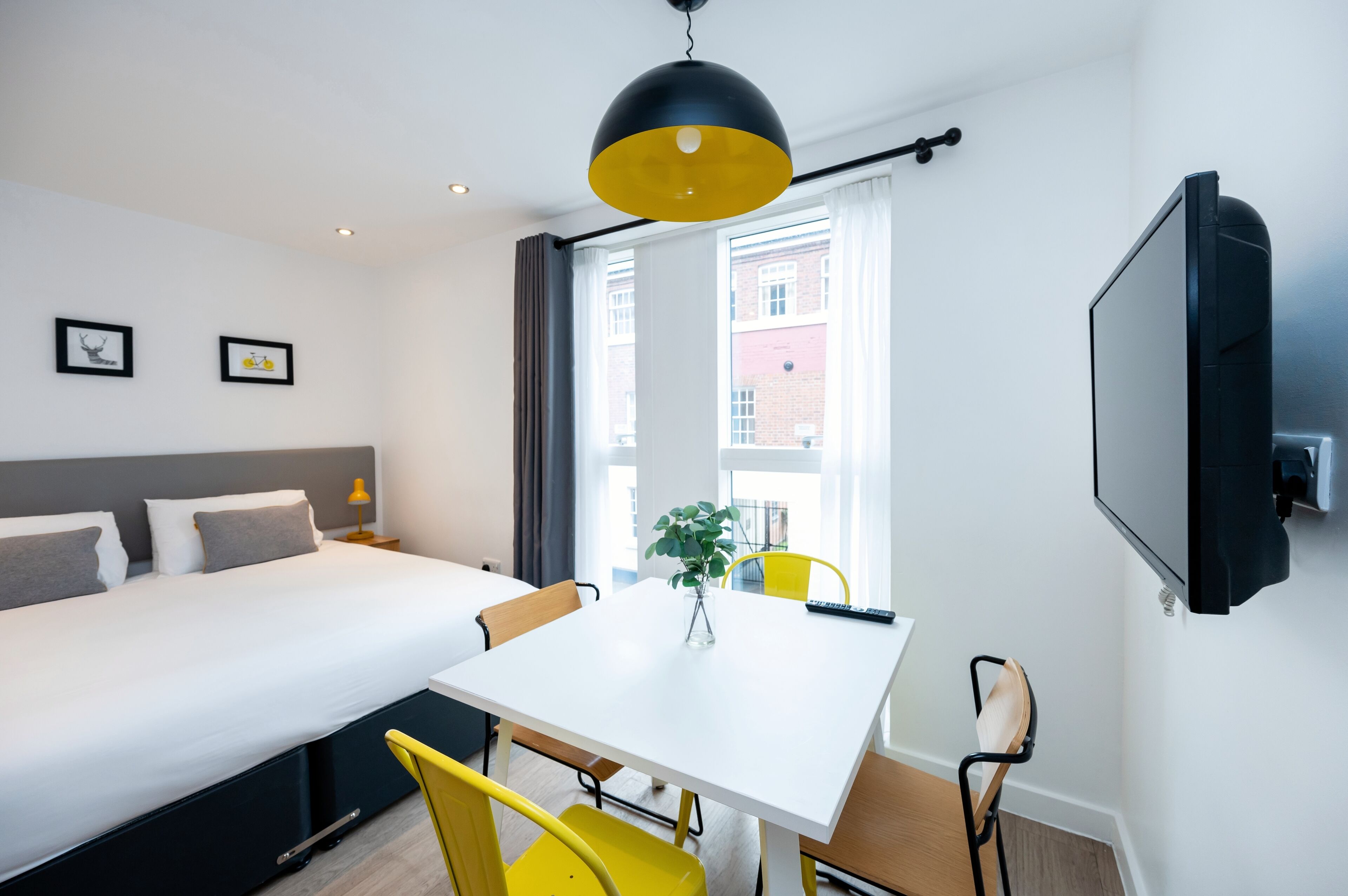 A modern hotel room with a bed, a dining table, and a TV.