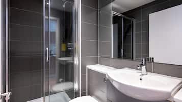 Un baño moderno con cabina de ducha de vidrio, inodoro blanco y un lavamanos grande con espejo superior.