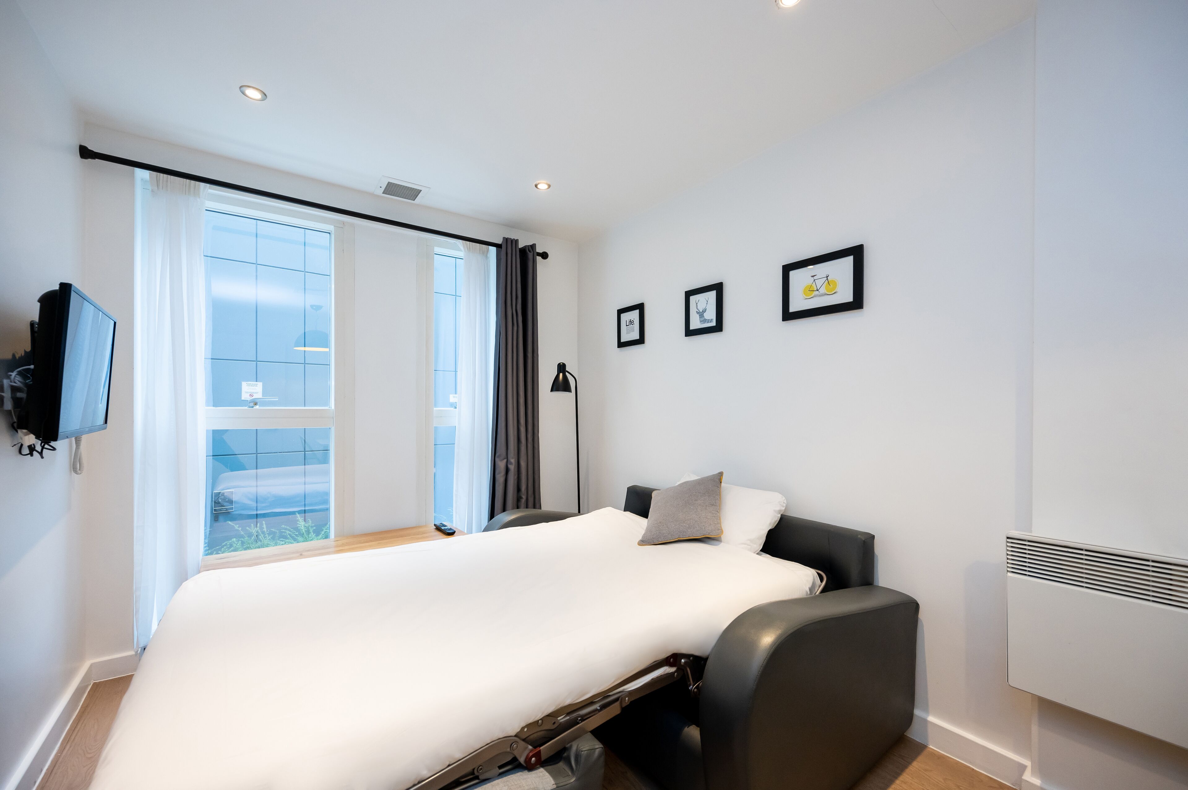 Een moderne hotelkamer met een groot bed, een flatscreen televisie, een raam met gordijnen en een wandradiator.