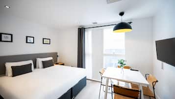 Una habitación de hotel moderna con una cama grande, una mesa de comedor con sillas, un televisor y cuadros en la pared.