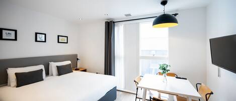 Una habitación de hotel moderna con una cama grande, una mesa de comedor con sillas, un televisor y cuadros en la pared.