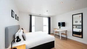Una habitació d'hotel moderna amb un llit gran, un escriptori, una cadira, un televisor i un mirall gran a la paret.
