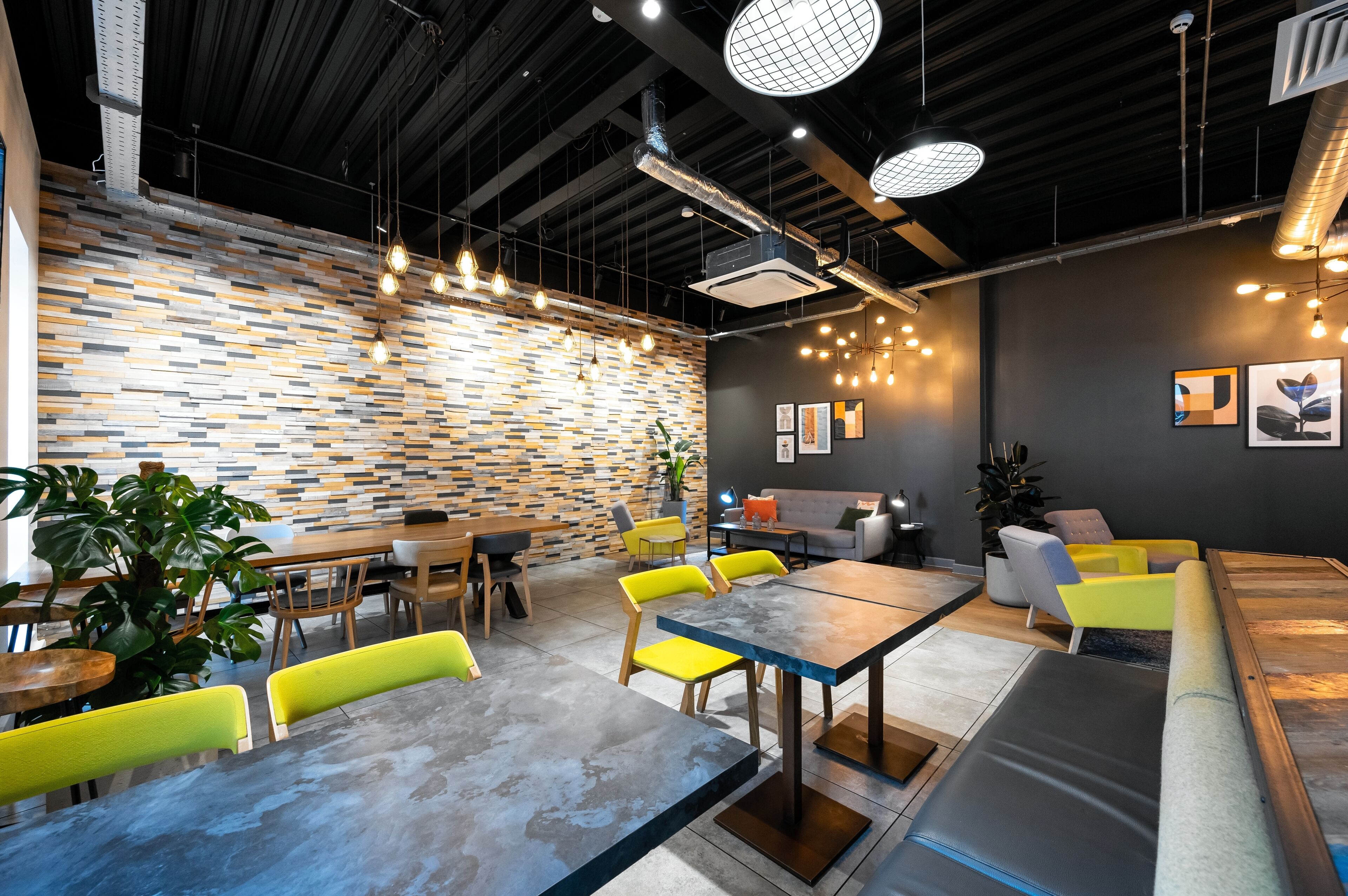 A modern interior with a brick-patterned wall, wooden tables, yellow chairs, and a gray sofa.