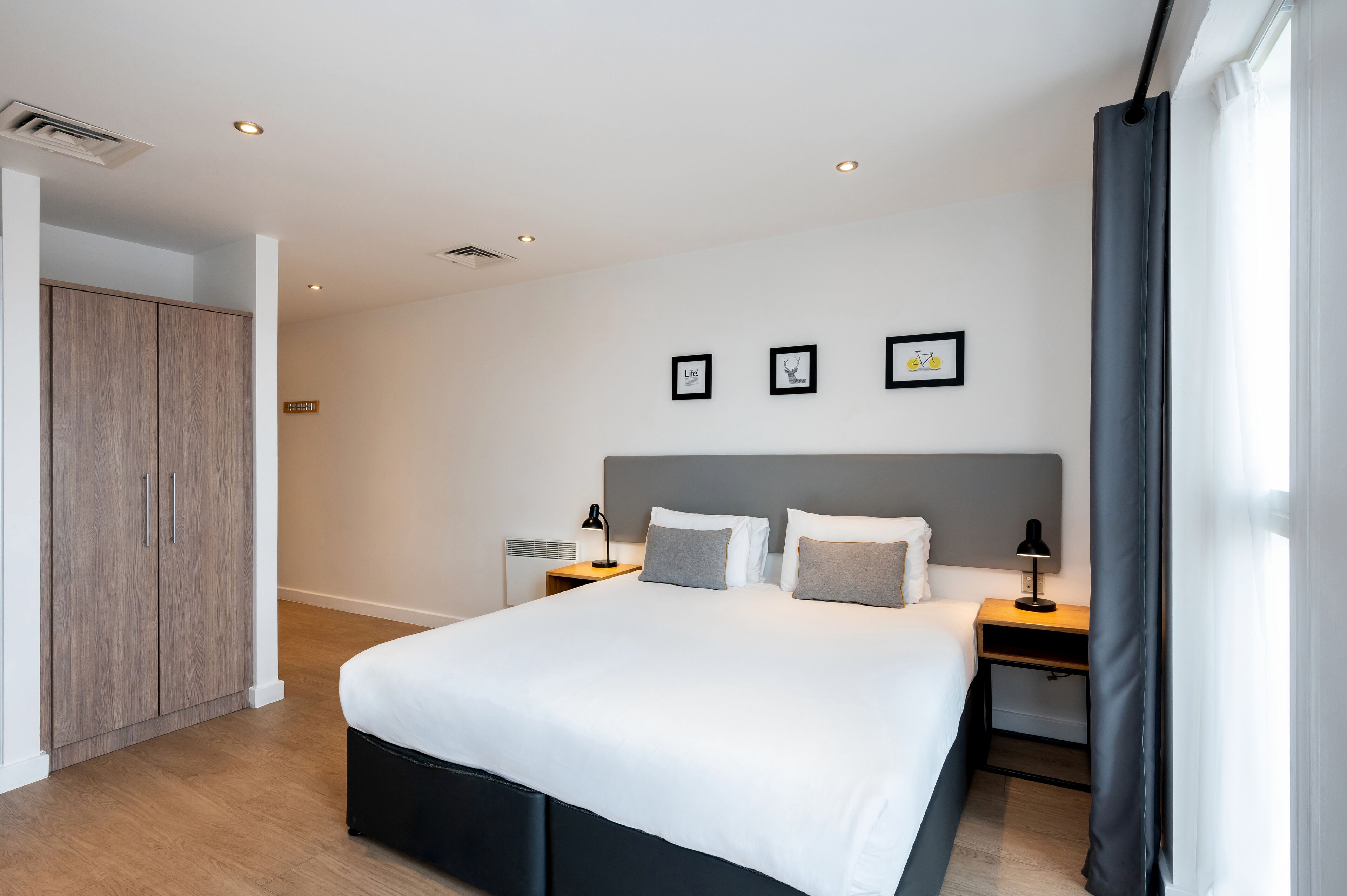A modern bedroom with a large bed, bedside tables, a wardrobe, and framed pictures on the wall.