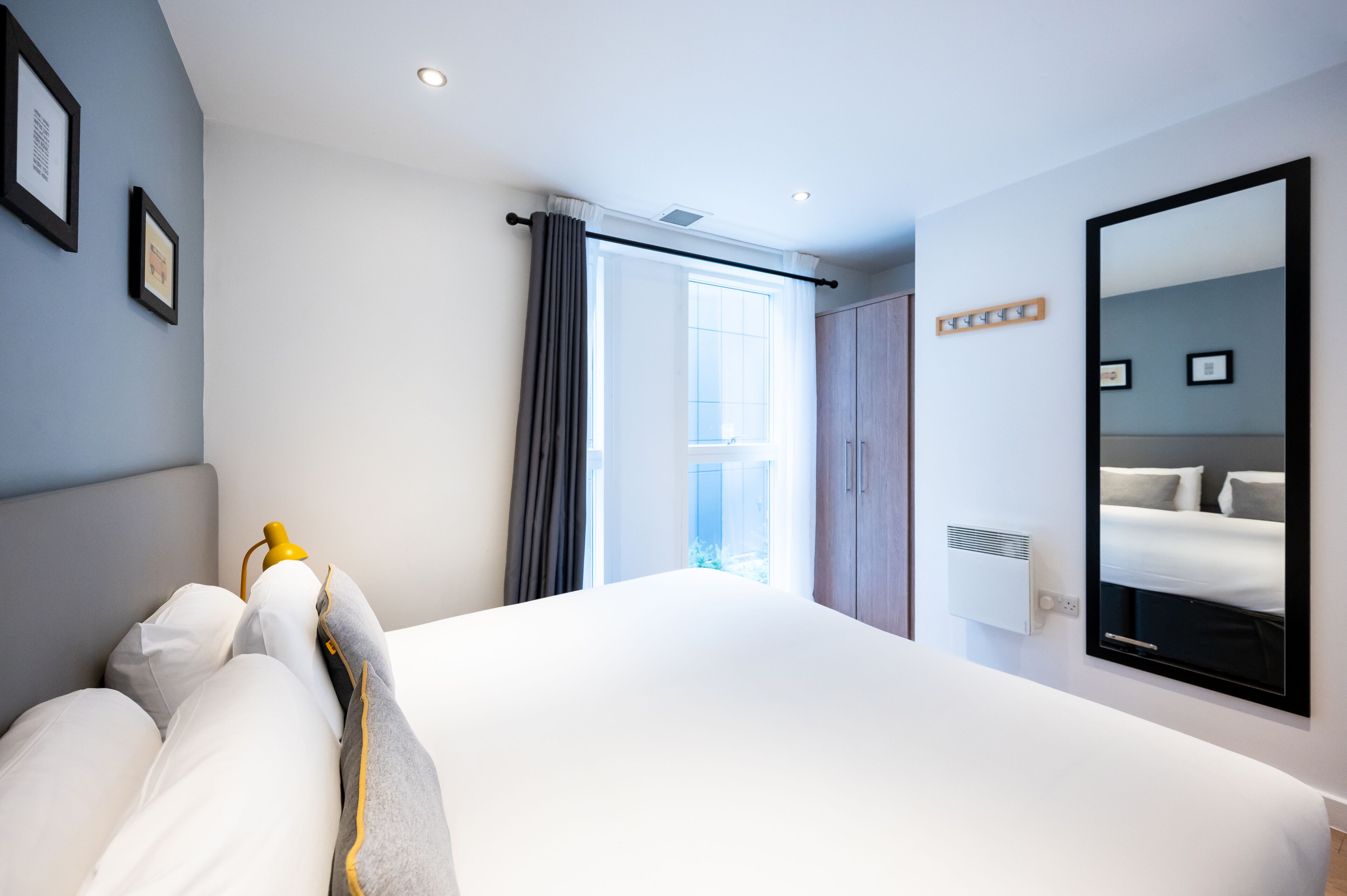 Habitación de hotel con una cama grande, un armario, un espejo y una ventana con cortinas.