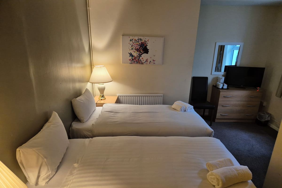 A hotel room with two beds, a lamp, a dresser, a TV, and a painting on the wall.