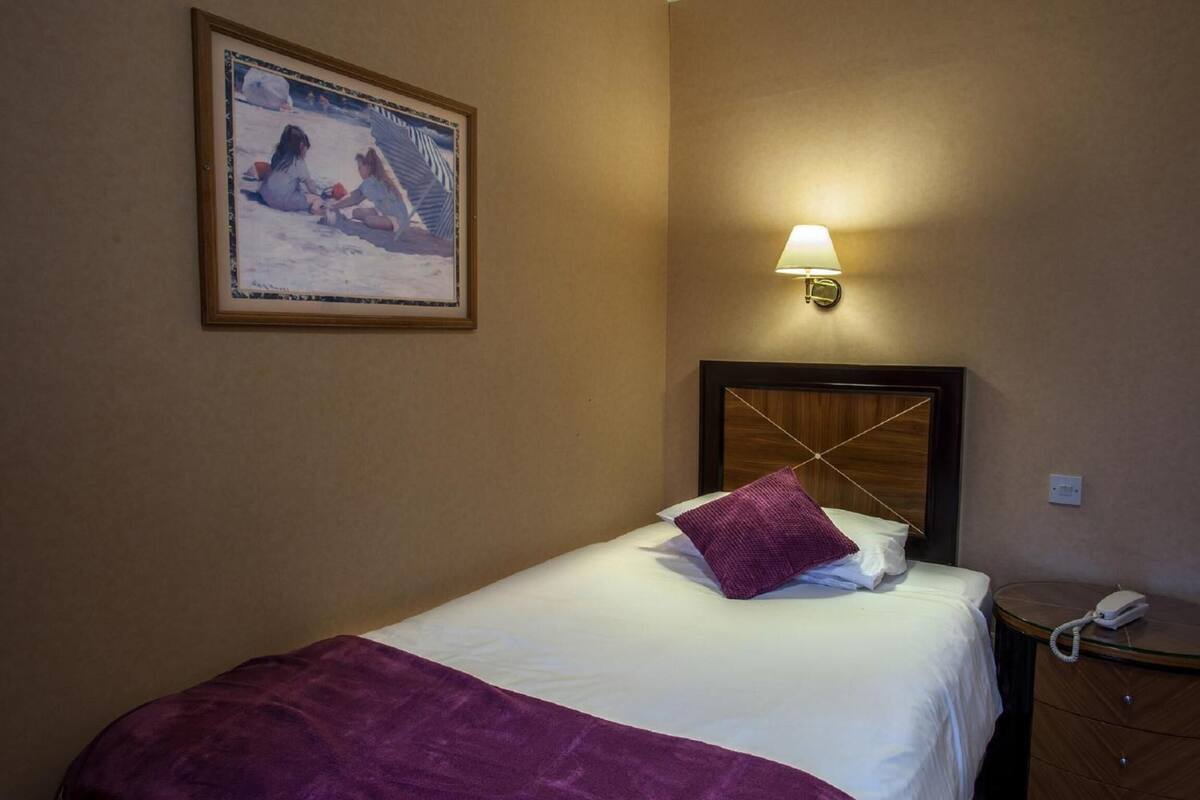 A hotel room with a bed, a nightstand, a lamp, and a framed picture on the wall.