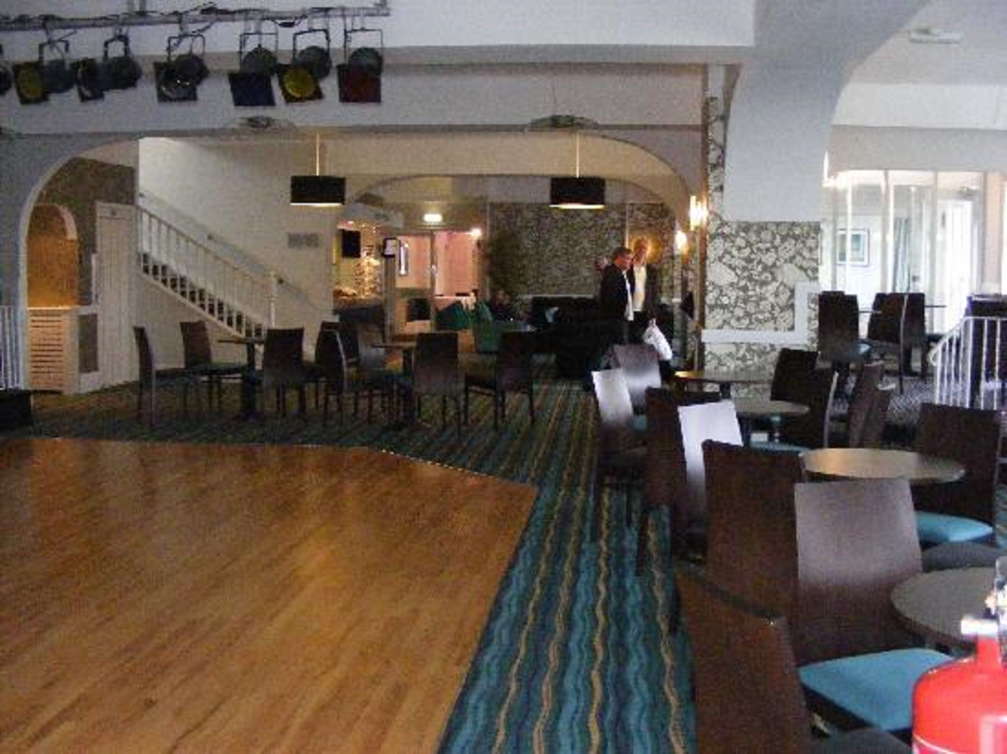 A spacious lobby with a wooden floor, blue patterned carpet, and multiple seating areas with chairs and tables.