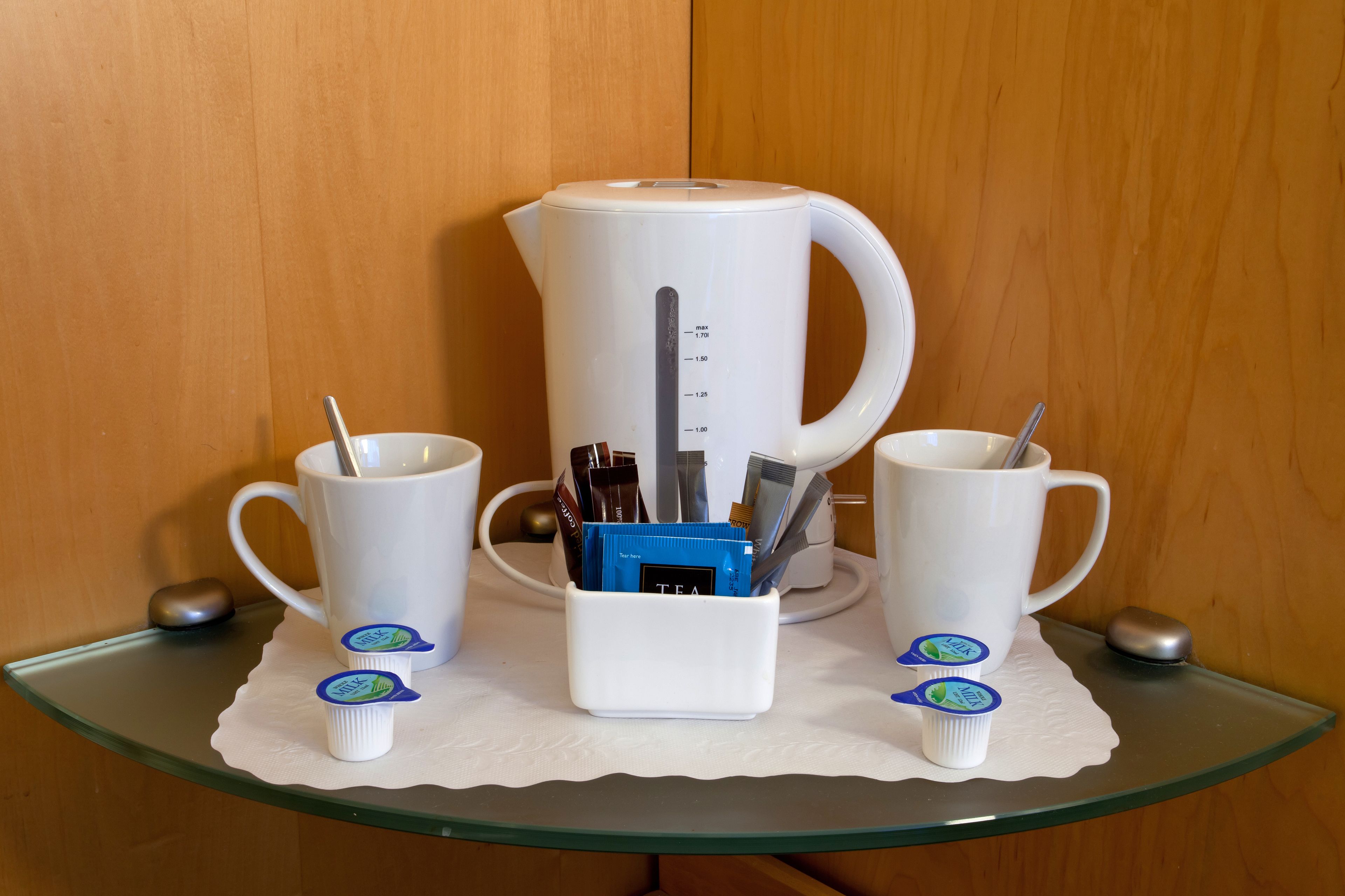 A coffee station with a white coffee maker, two white cups, and a white mug on a glass table.