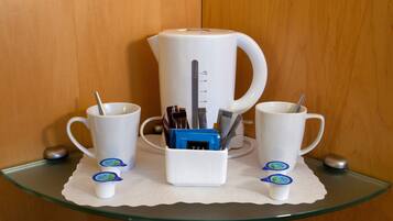 A coffee station with a white coffee maker, two white cups, and a white mug on a glass table.