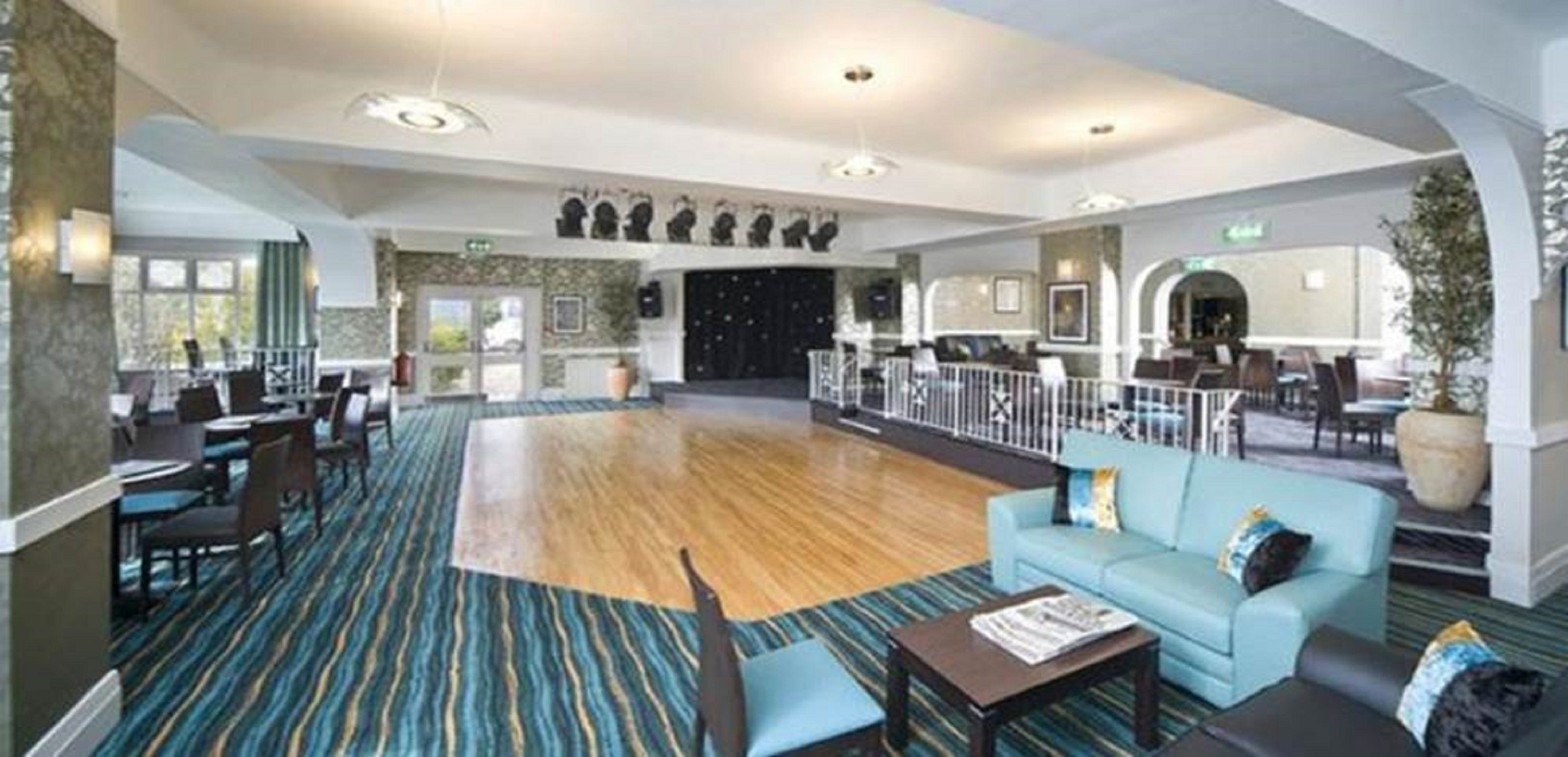 A spacious lobby with a wooden floor, a blue sofa, and a dining area with tables and chairs.