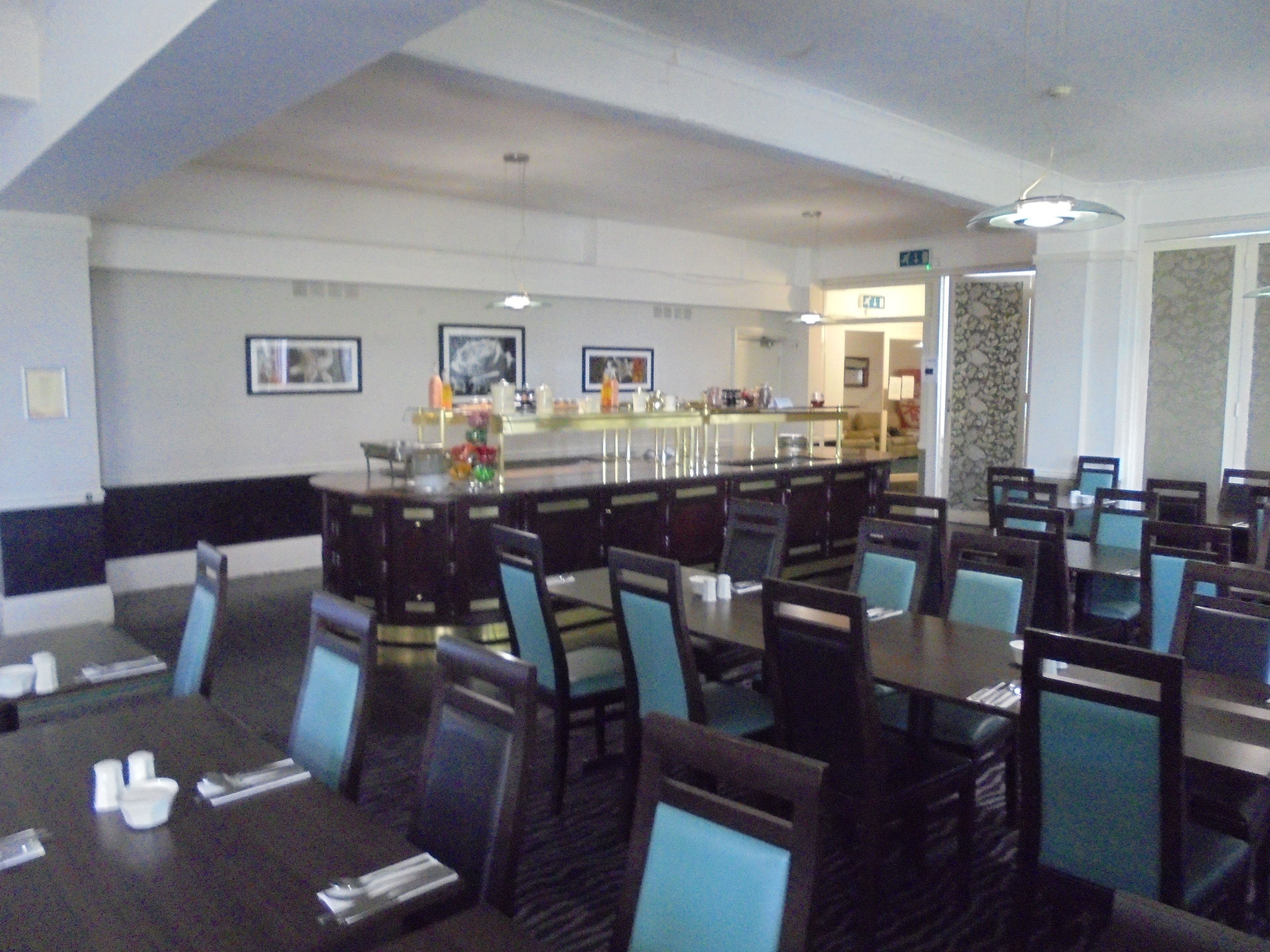 A spacious dining area with multiple tables and chairs, a central bar, and framed artwork on the walls.