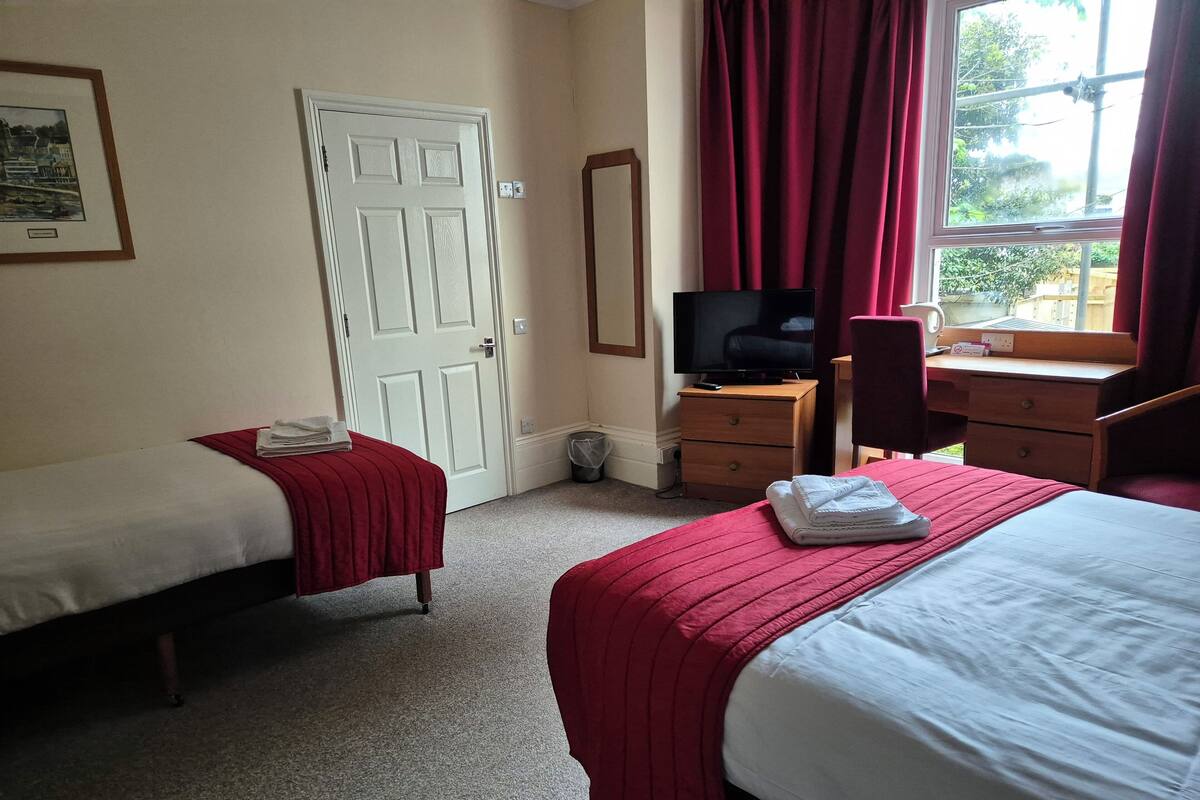 A hotel room with two beds, a television, a desk with a chair, and a window with curtains.